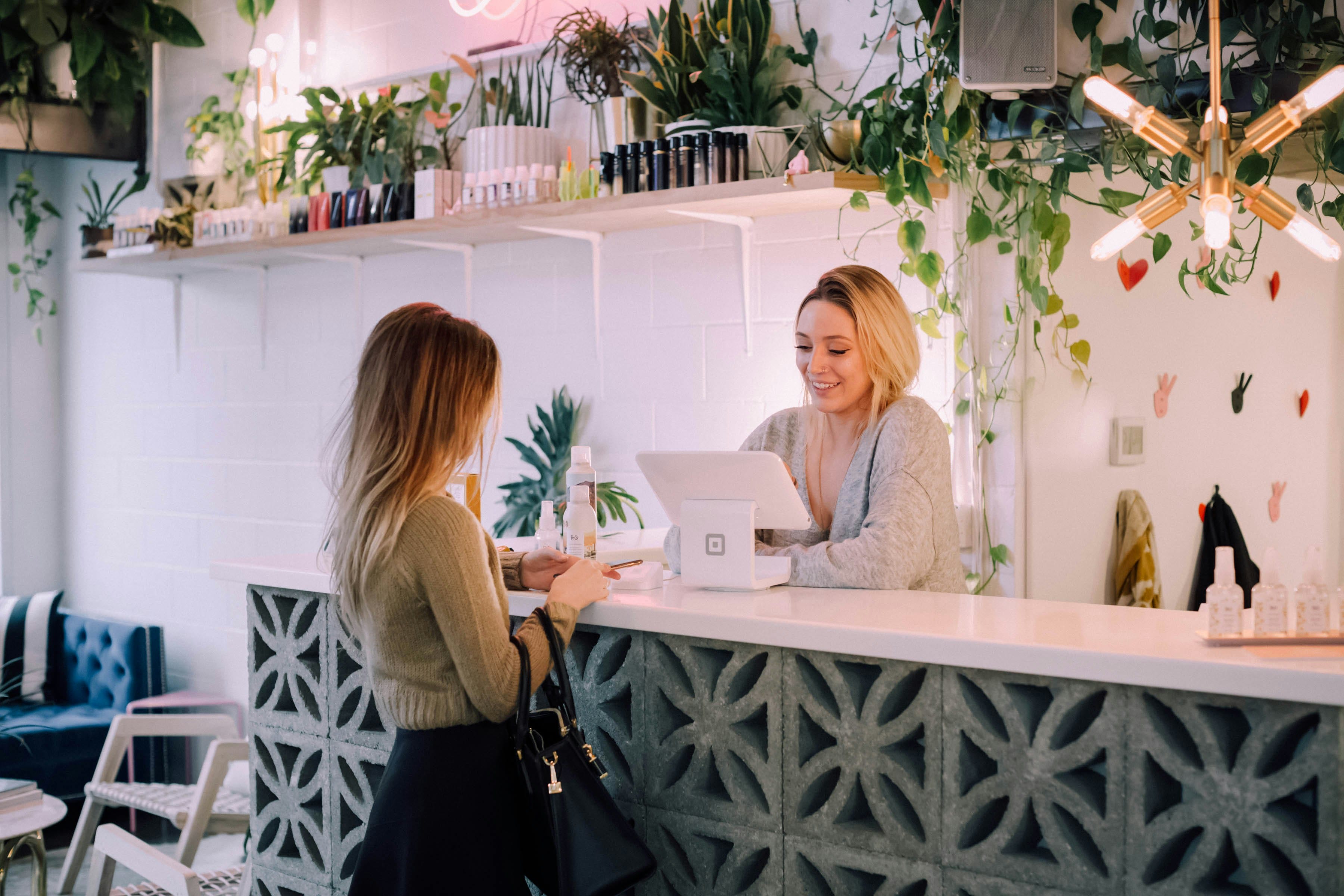 Two women interacting at a beauty salon counter.